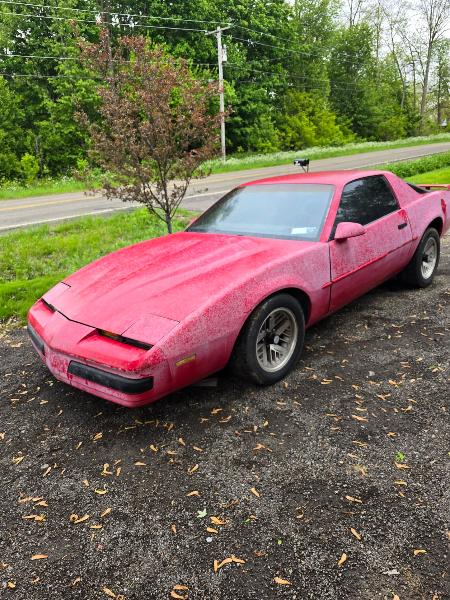 Faded red non-running sports car parked on gravel awaiting pickup