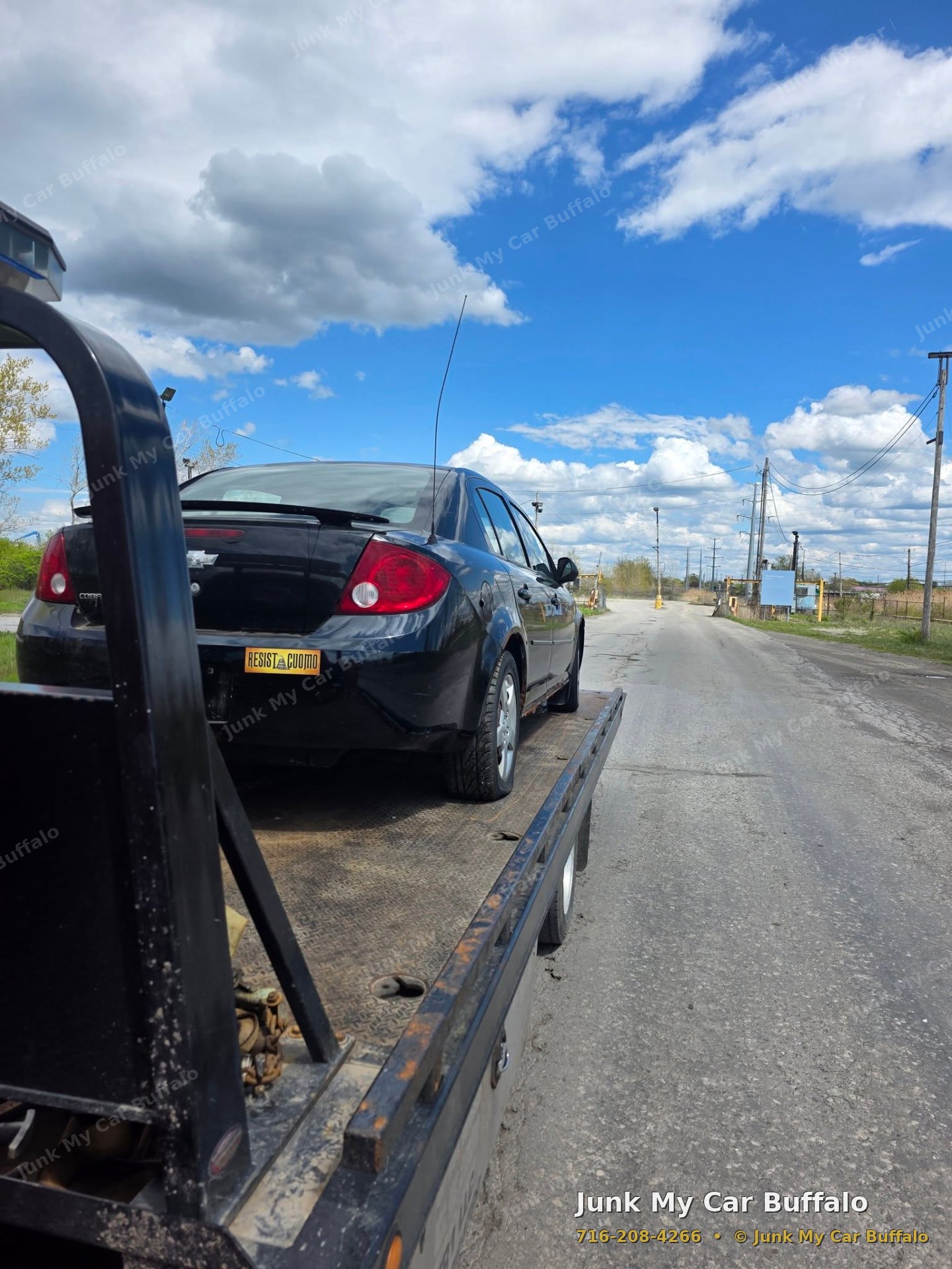 Black sedan loaded on a flatbed tow truck for junk car removal in Buffalo, NY