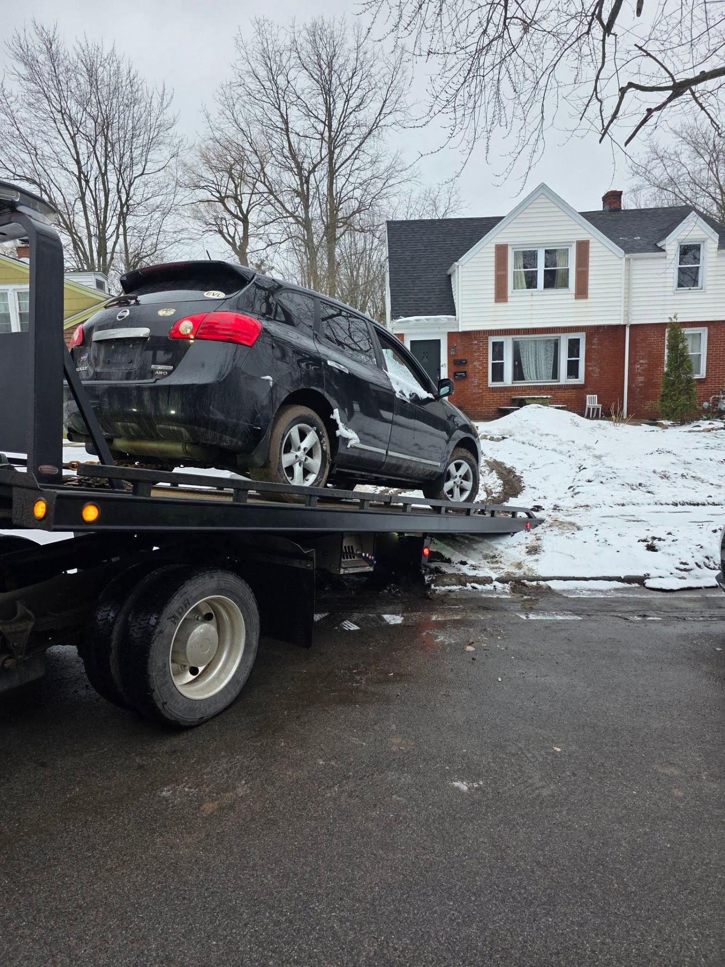 Black SUV loaded on a flatbed tow truck during a Buffalo winter pickup