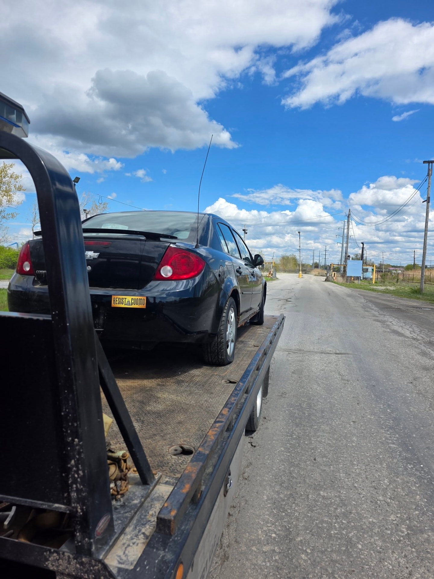 Black sedan loaded on a flatbed tow truck for junk car removal in Buffalo, NY